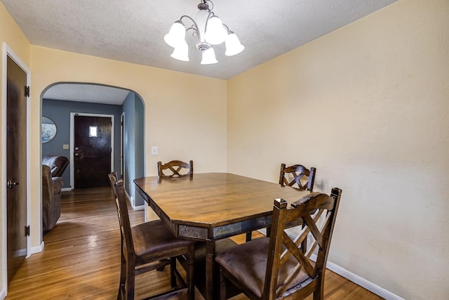 dining area with a textured ceiling, a notable chandelier, and dark wood-type flooring