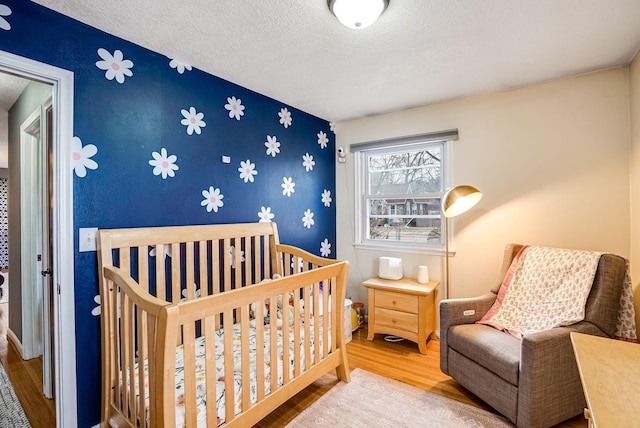 bedroom with a crib, wood-type flooring, and a textured ceiling