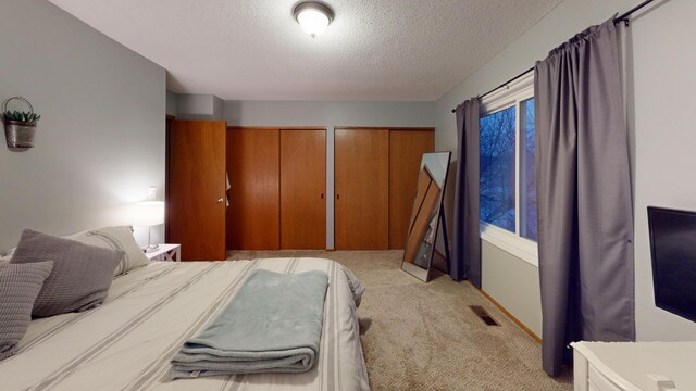 bedroom featuring two closets, a textured ceiling, and light colored carpet