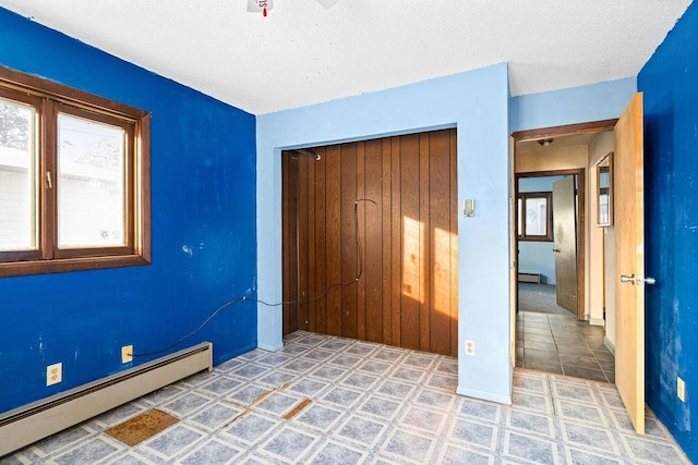 unfurnished bedroom featuring a textured ceiling, a baseboard radiator, and a closet