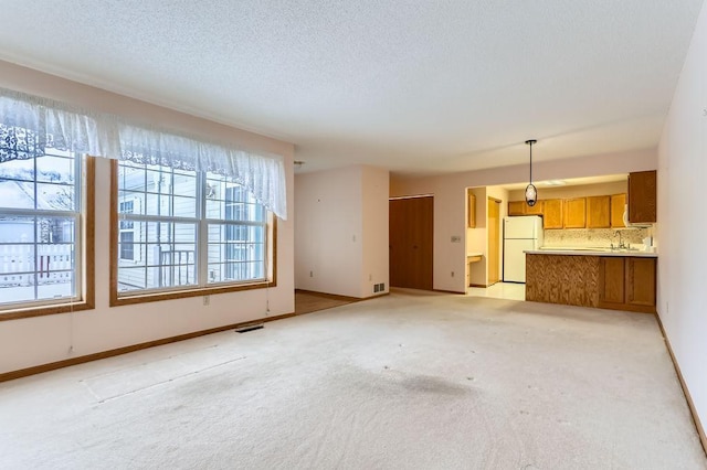 unfurnished living room featuring sink, light colored carpet, and a textured ceiling