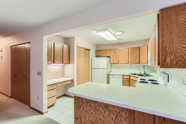 kitchen with built in desk, light countertops, a sink, white appliances, and a peninsula