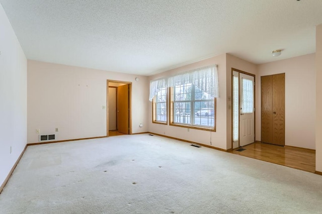 unfurnished room with a textured ceiling, baseboards, visible vents, and light colored carpet