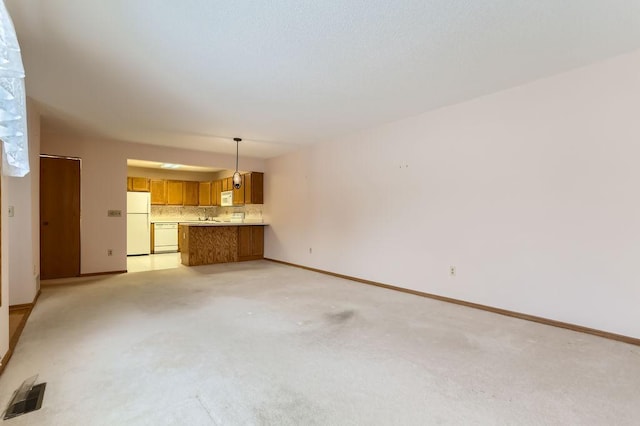 unfurnished living room with light colored carpet, visible vents, a sink, and baseboards