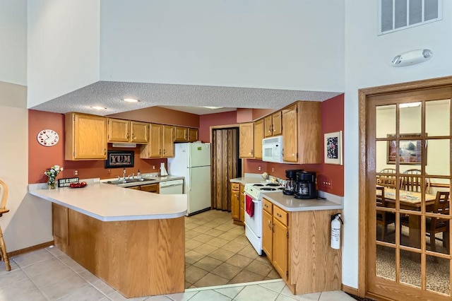 kitchen with a peninsula, white appliances, visible vents, light countertops, and brown cabinetry