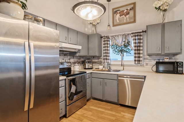 kitchen with backsplash, sink, gray cabinets, light wood-type flooring, and appliances with stainless steel finishes