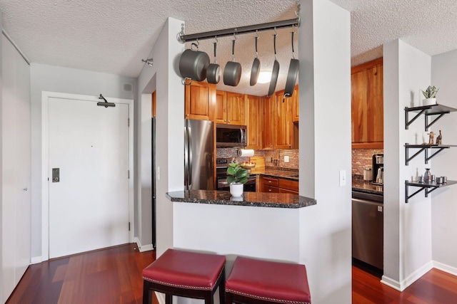 kitchen with dark stone counters, tasteful backsplash, stainless steel appliances, and a textured ceiling