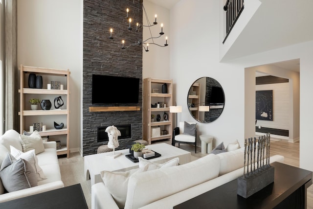 living room with a stone fireplace, light wood-type flooring, a towering ceiling, and an inviting chandelier