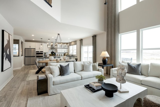 living room with an inviting chandelier, a high ceiling, and light wood-type flooring