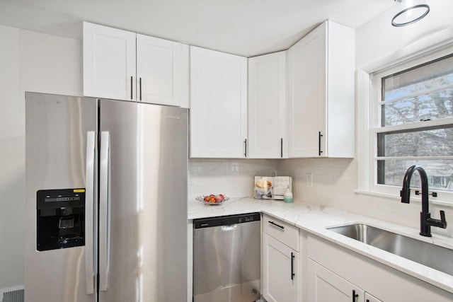 kitchen featuring white cabinets, sink, decorative backsplash, light stone counters, and stainless steel appliances