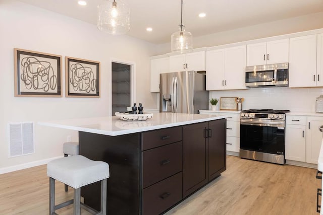 kitchen featuring white cabinetry, decorative light fixtures, stainless steel appliances, and a center island