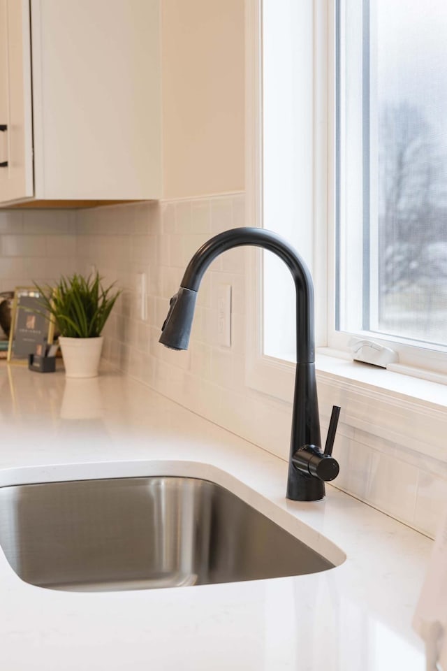 room details featuring sink, decorative backsplash, and white cabinets