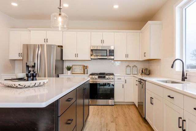 kitchen with sink, appliances with stainless steel finishes, plenty of natural light, white cabinets, and decorative light fixtures