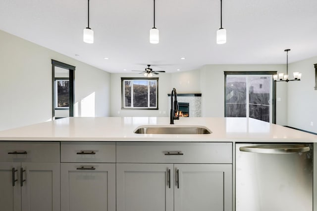 kitchen featuring stainless steel dishwasher, a sink, light countertops, gray cabinetry, and hanging light fixtures