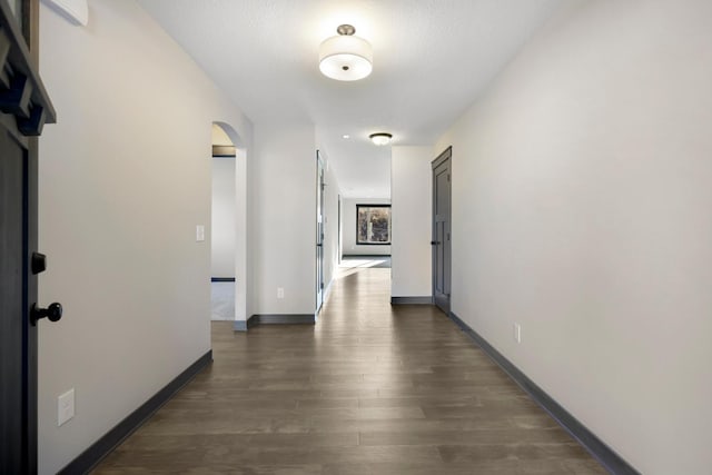 hallway with arched walkways, dark wood-style flooring, and baseboards