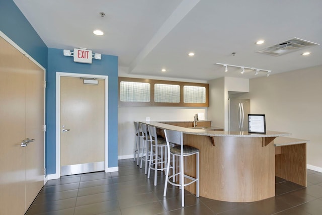 kitchen with dark tile patterned flooring, sink, stainless steel fridge, kitchen peninsula, and a breakfast bar area