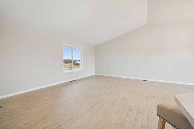 empty room with lofted ceiling, light wood-style flooring, and baseboards