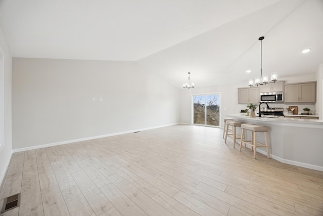 living area featuring lofted ceiling, a notable chandelier, visible vents, baseboards, and light wood finished floors