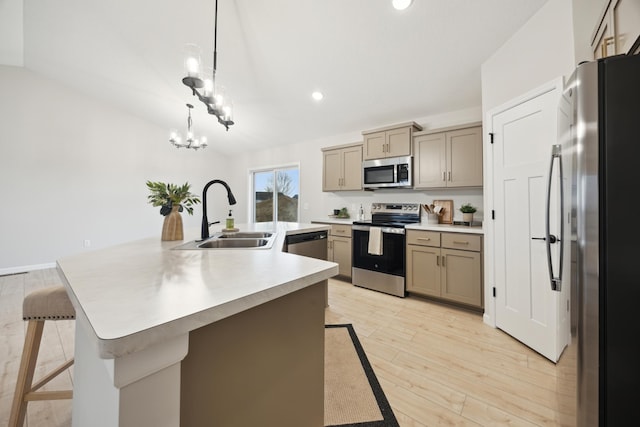 kitchen with a breakfast bar area, a kitchen island with sink, light wood-style flooring, a sink, and appliances with stainless steel finishes