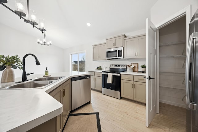 kitchen featuring stainless steel appliances, a sink, light wood-style floors, light countertops, and decorative light fixtures