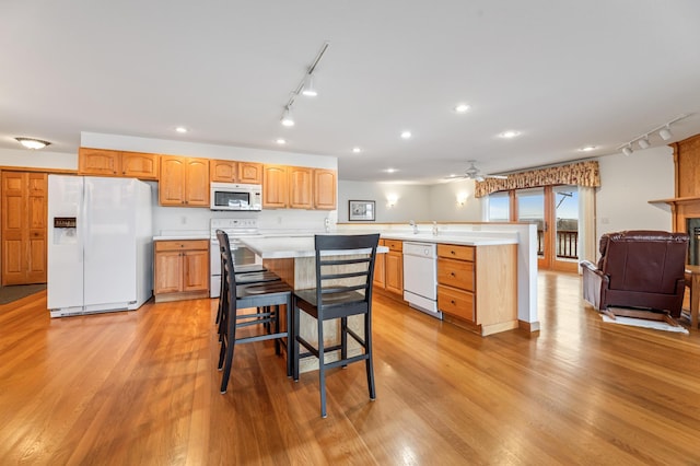 kitchen featuring ceiling fan, white appliances, a kitchen bar, a kitchen island, and light wood-type flooring