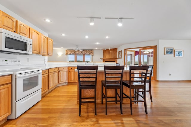 kitchen featuring a center island, white appliances, a kitchen breakfast bar, ceiling fan, and light hardwood / wood-style floors