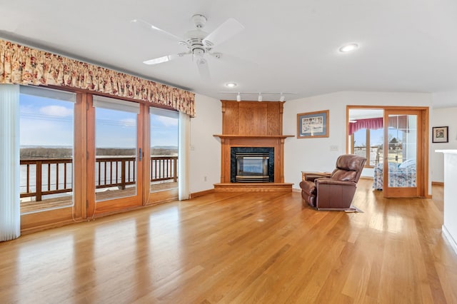 unfurnished living room with ceiling fan, a premium fireplace, track lighting, and light hardwood / wood-style flooring