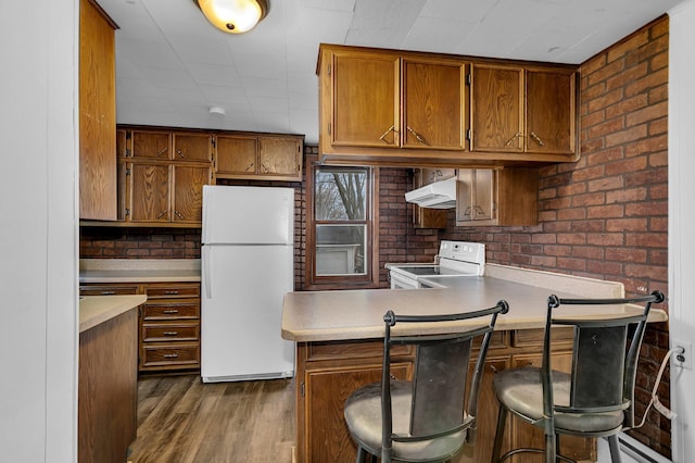 kitchen with kitchen peninsula, brick wall, a breakfast bar, white appliances, and dark wood-type flooring