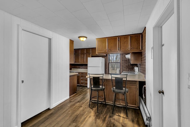 kitchen featuring tasteful backsplash, a breakfast bar, a baseboard heating unit, dark wood-type flooring, and white fridge