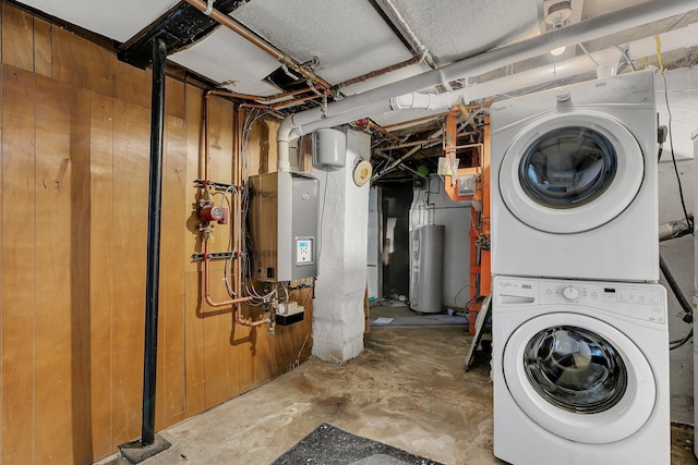 clothes washing area with wood walls, stacked washer and dryer, and water heater