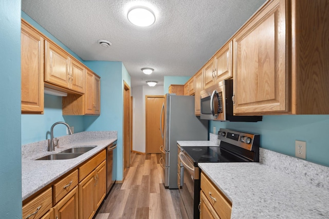 kitchen with a textured ceiling, sink, appliances with stainless steel finishes, and light hardwood / wood-style flooring