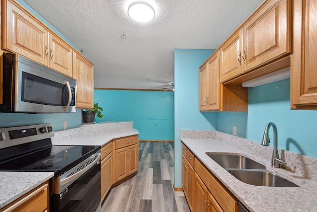 kitchen with sink, stainless steel appliances, a textured ceiling, and light hardwood / wood-style floors