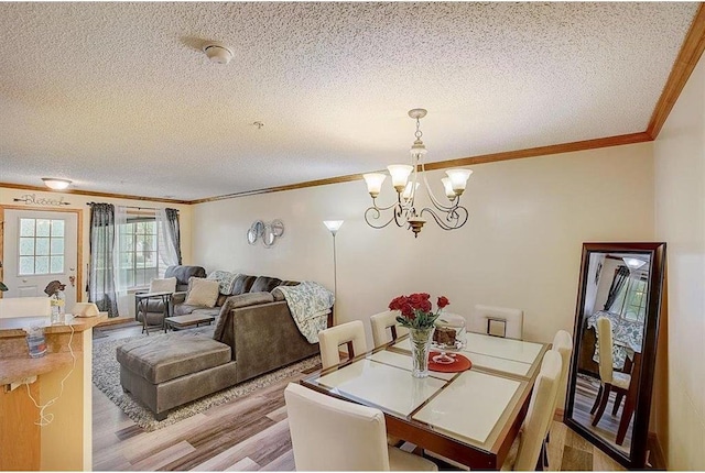 dining area featuring light hardwood / wood-style floors, ornamental molding, a textured ceiling, and a chandelier