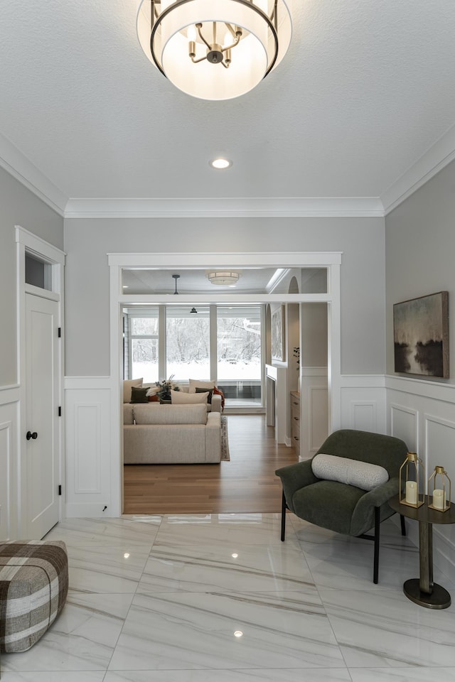 interior space with a wainscoted wall, marble finish floor, a decorative wall, and crown molding