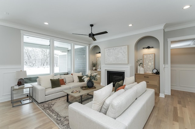 living room with ornamental molding, a glass covered fireplace, light wood finished floors, and recessed lighting