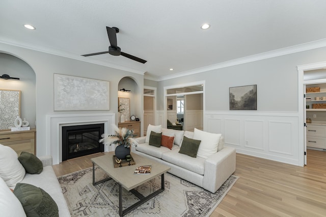 living room with a wainscoted wall, recessed lighting, ornamental molding, a glass covered fireplace, and light wood-type flooring