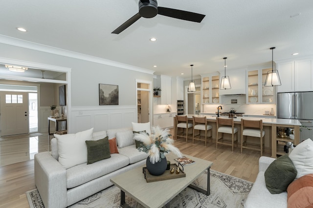 living room featuring crown molding, light wood finished floors, recessed lighting, a ceiling fan, and wainscoting