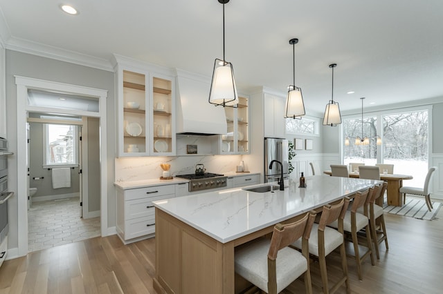 kitchen featuring a breakfast bar, a sink, light wood-style floors, appliances with stainless steel finishes, and an island with sink