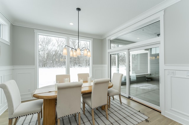 dining space featuring a wainscoted wall, crown molding, a decorative wall, a chandelier, and light wood-type flooring