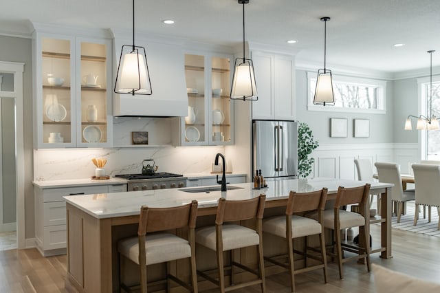 kitchen with a center island with sink, backsplash, stove, freestanding refrigerator, and a sink