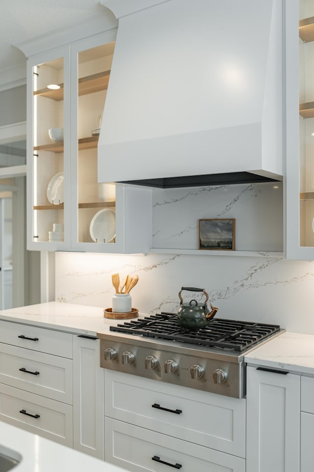 kitchen featuring white cabinets, stainless steel gas stovetop, glass insert cabinets, and custom range hood