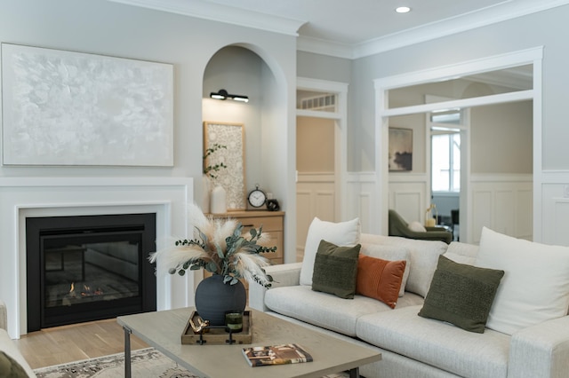 living area with crown molding, recessed lighting, light wood-style floors, a glass covered fireplace, and wainscoting