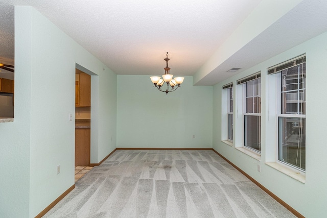 spare room with an inviting chandelier, light carpet, and a textured ceiling