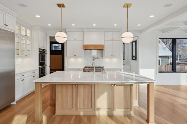 kitchen with white cabinets, appliances with stainless steel finishes, light hardwood / wood-style flooring, and a spacious island