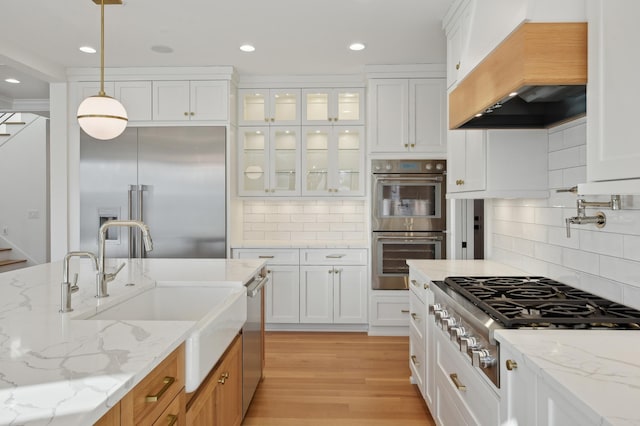 kitchen with light stone counters, white cabinets, stainless steel appliances, and custom range hood