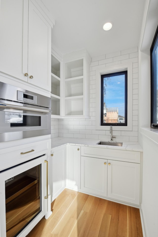 kitchen with light wood-type flooring, light stone counters, sink, white cabinets, and oven