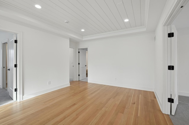 empty room featuring light wood-type flooring, a raised ceiling, and wooden ceiling