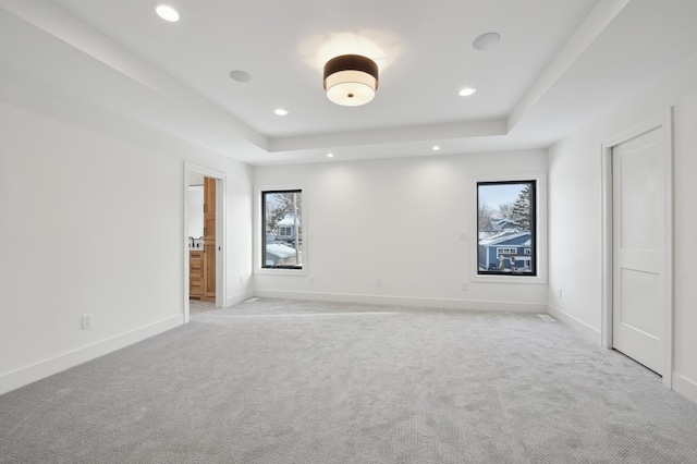 unfurnished bedroom with light colored carpet, a raised ceiling, and ensuite bathroom