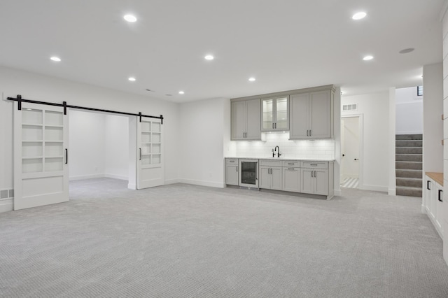 interior space with a barn door, light carpet, sink, and wine cooler