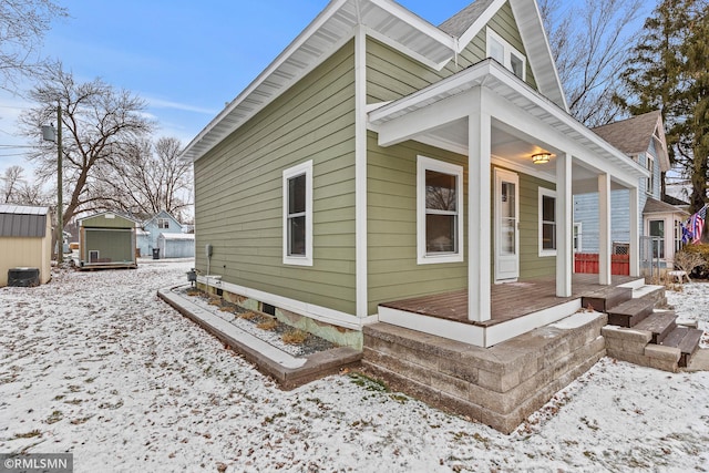 view of snow covered exterior featuring a porch and a storage unit